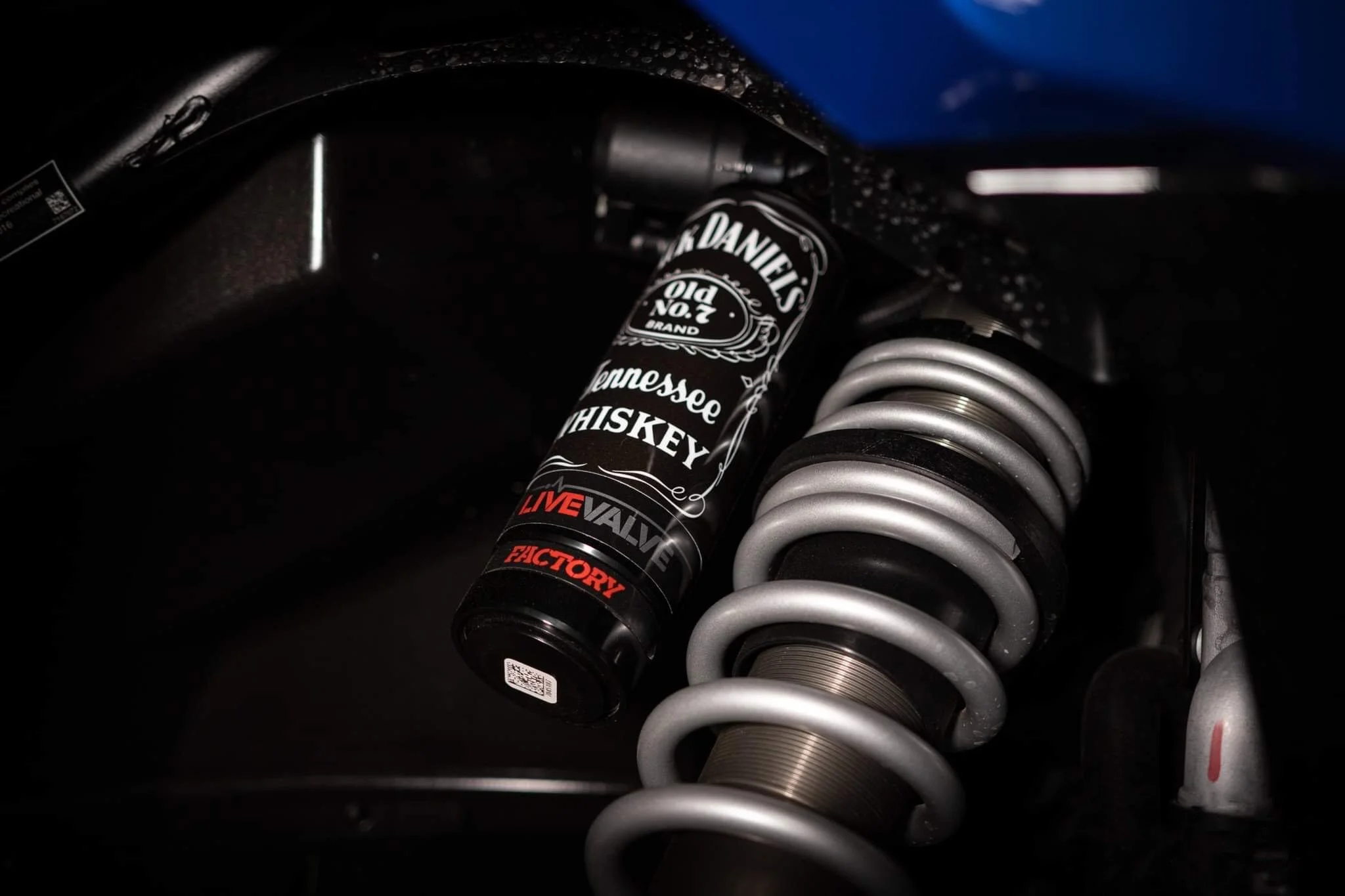 Close-up of a motorcycle suspension system with a coil spring and a can of Jack Daniel's Tennessee whiskey attached nearby.