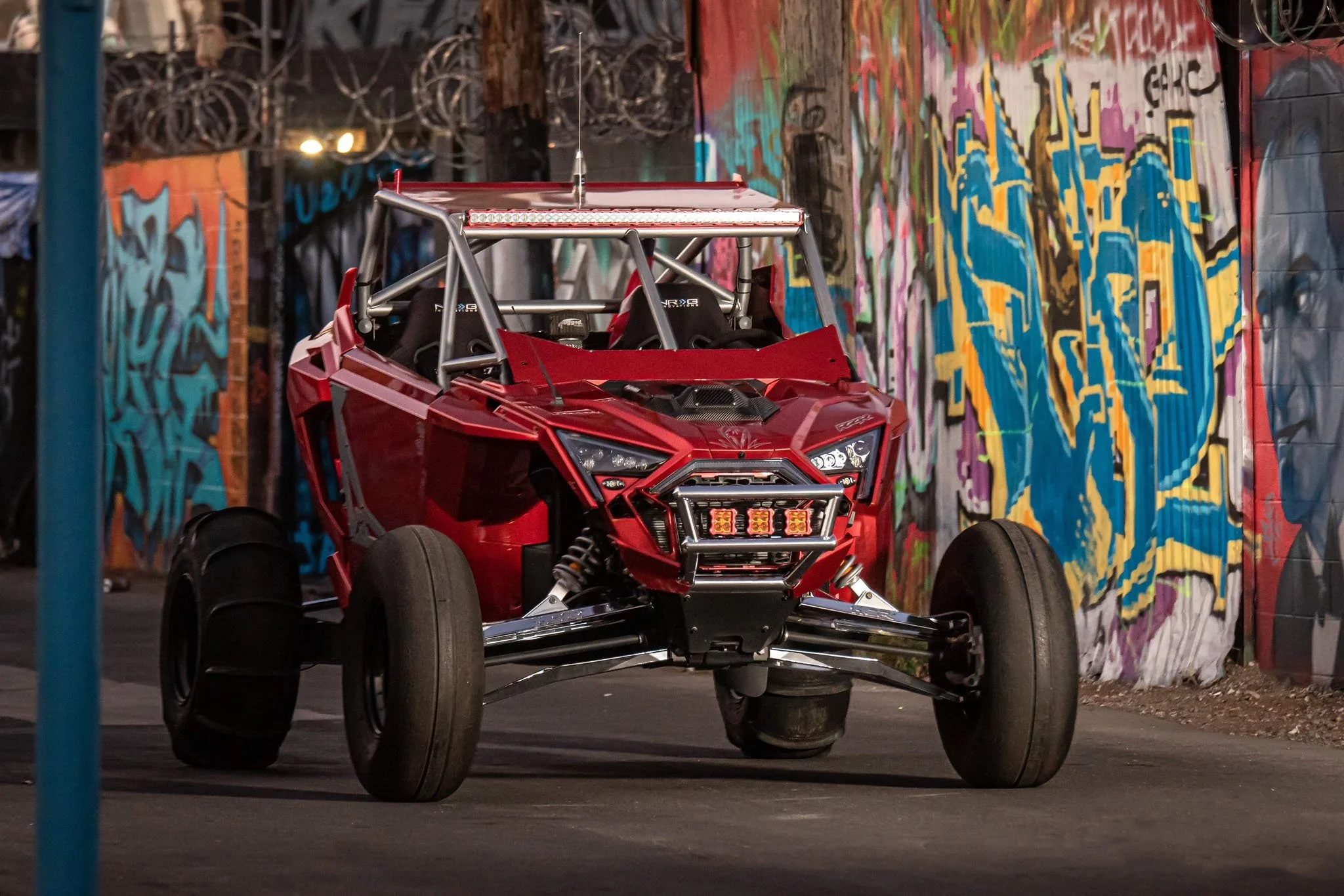 Red off-road racing vehicle parked in front of a colorful graffiti-covered wall.