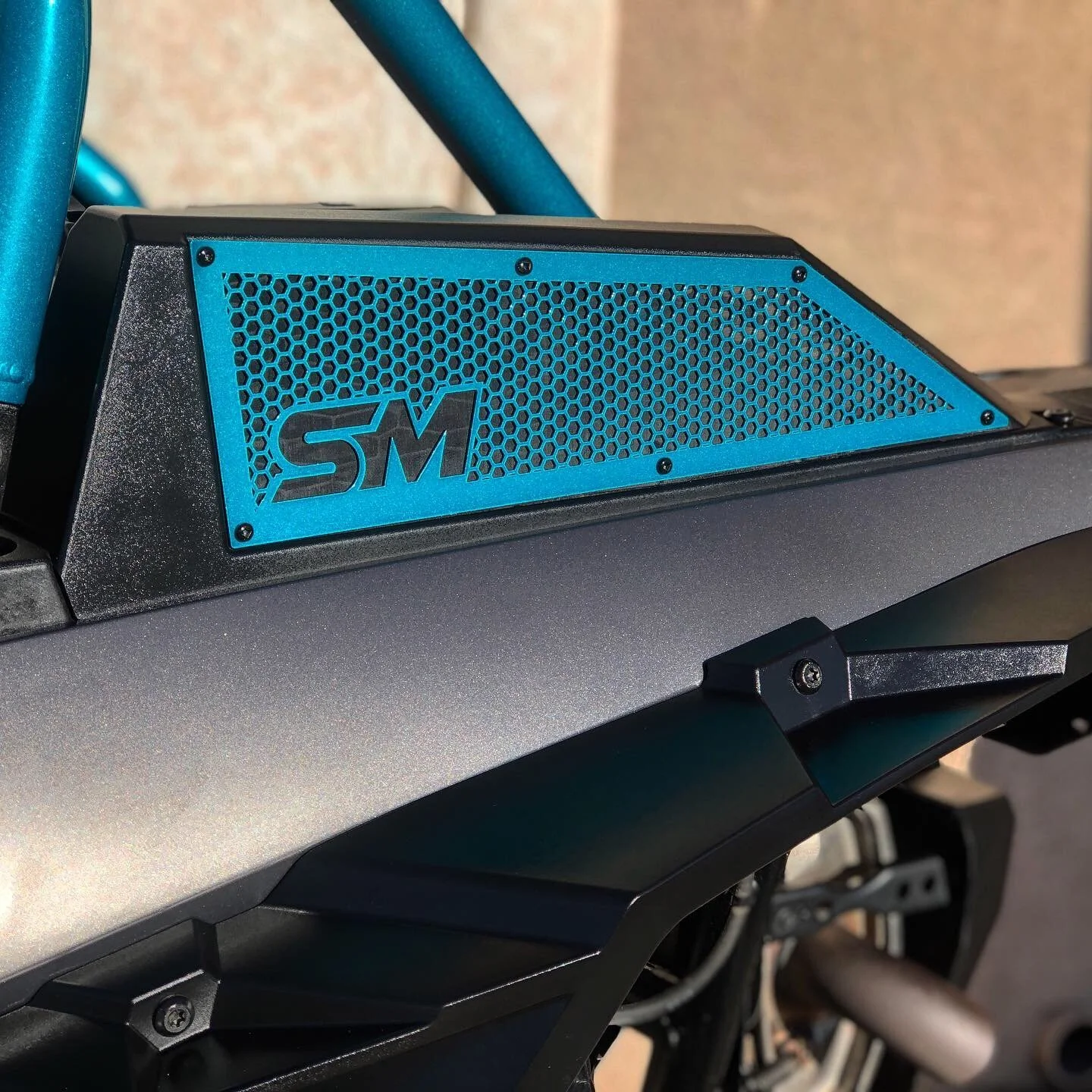 Close-up of a blue protective grille with the letters "SM" on a motorcycle