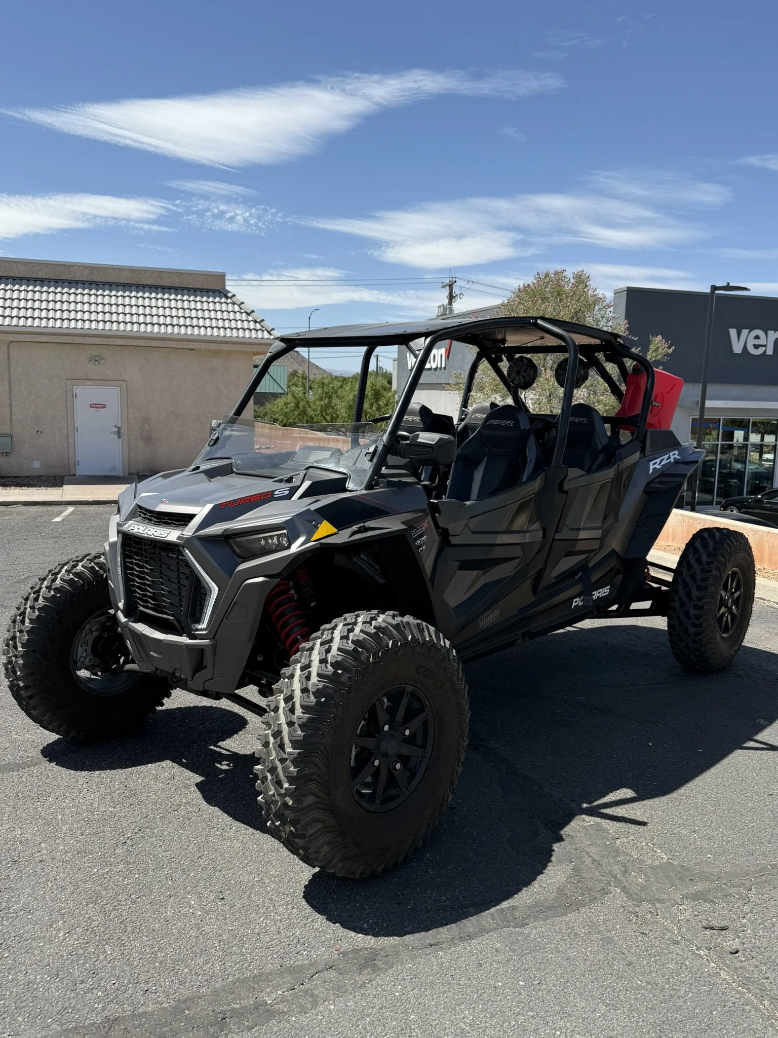 Close-up of a black off-road vehicle with a prominent grille and Suspension, parked in front of a business sign that reads Custom Sans Motor Sports, specializing in custom off-road vehicles.