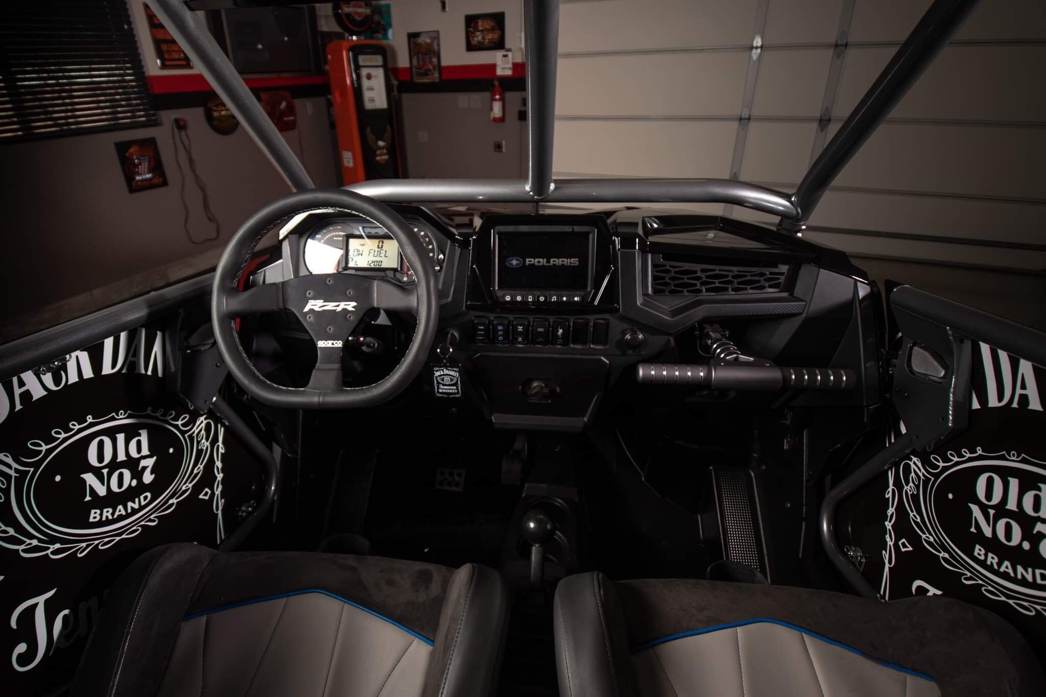 Interior view of a Polaris off-road vehicle, showing a steering wheel, digital dashboard, and various control switches.