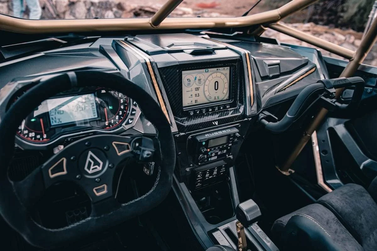 Interior of a rugged off-road vehicle with a digital dashboard and multiple control panels, including a steering wheel, digital display, and gear shifter.