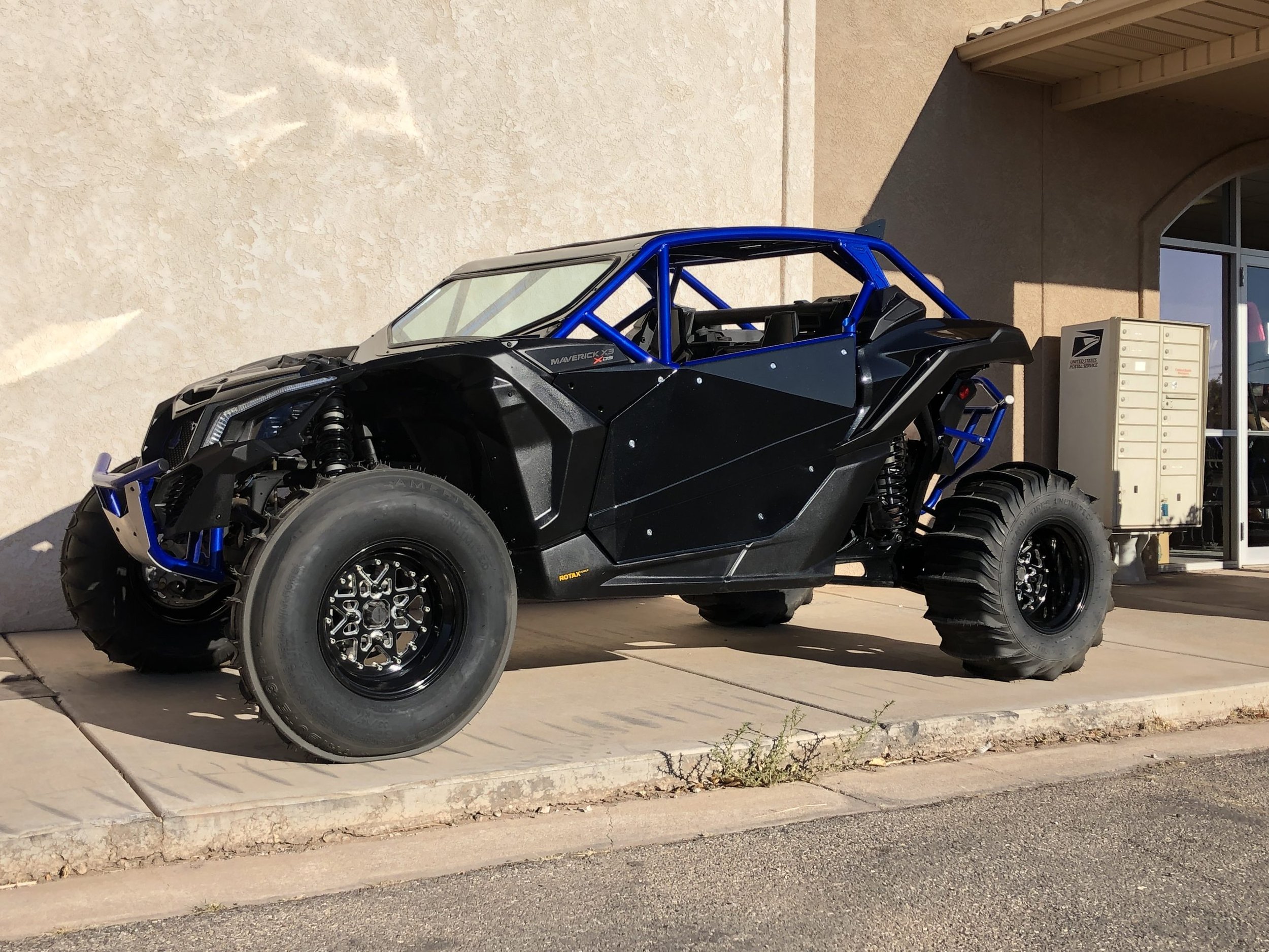 Off-road race car with black body and blue roll cage parked outside a building.