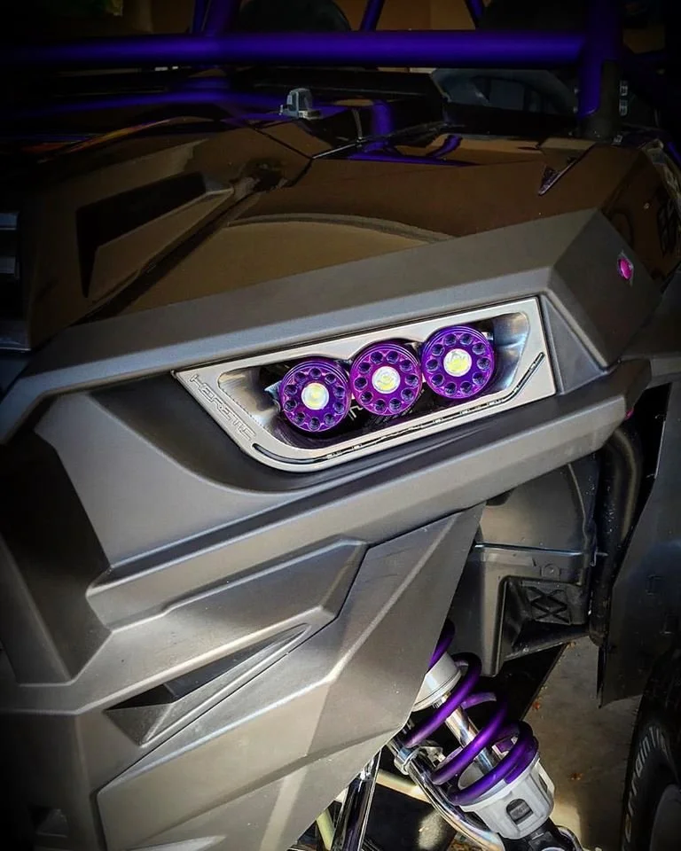 Close-up of a motorcycle's front with purple LED lights in the headlight area and purple suspension springs.