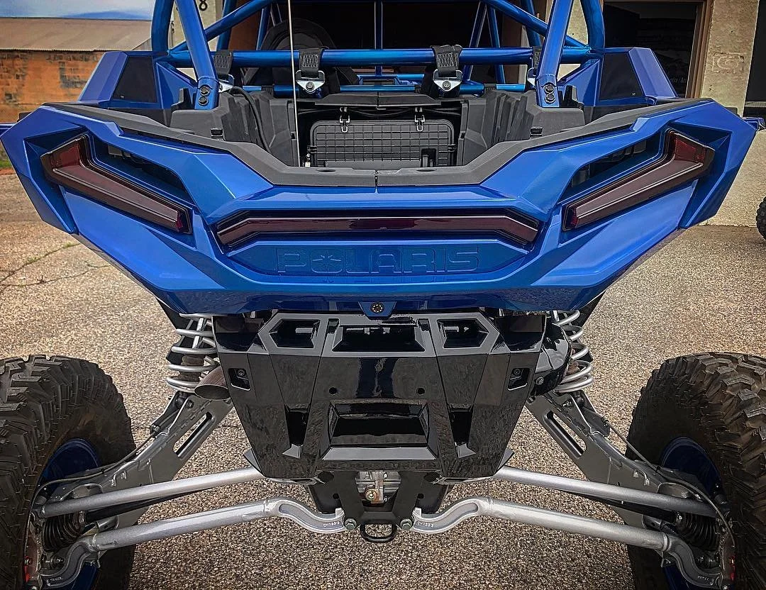 Front view of a blue Polaris off-road vehicle with exposed suspension components and large off-road tires.