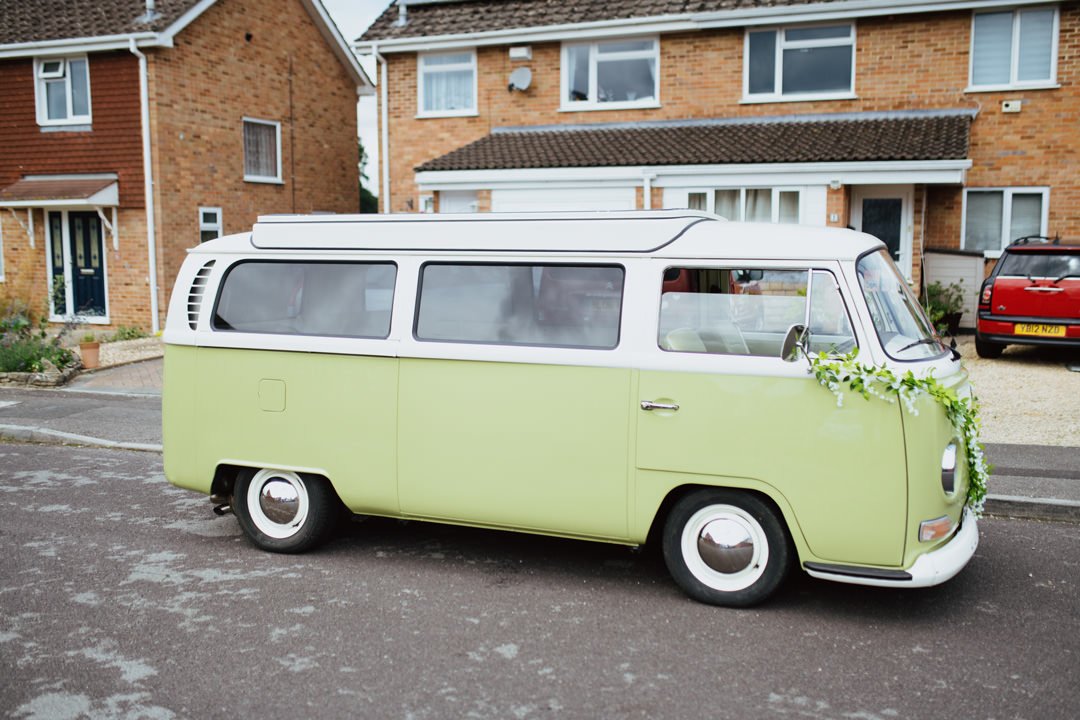 olive green vw camper van parked on street outside of houses. there are flowers on the bonnet