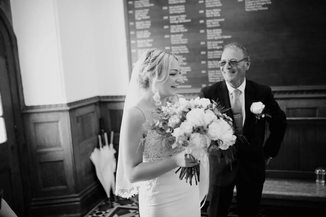 wedding bride holding flowers smiling stood next to her father.
