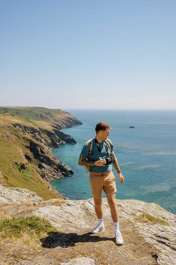 Somerset wedding photographer Benjamin standing on the South West Coast Path with his camera overlooking the coastline.