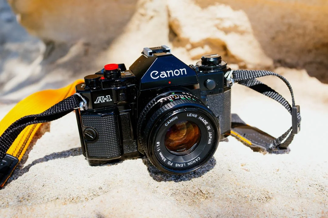 canon a-1 film camera on rock in sunlight with yellow strap