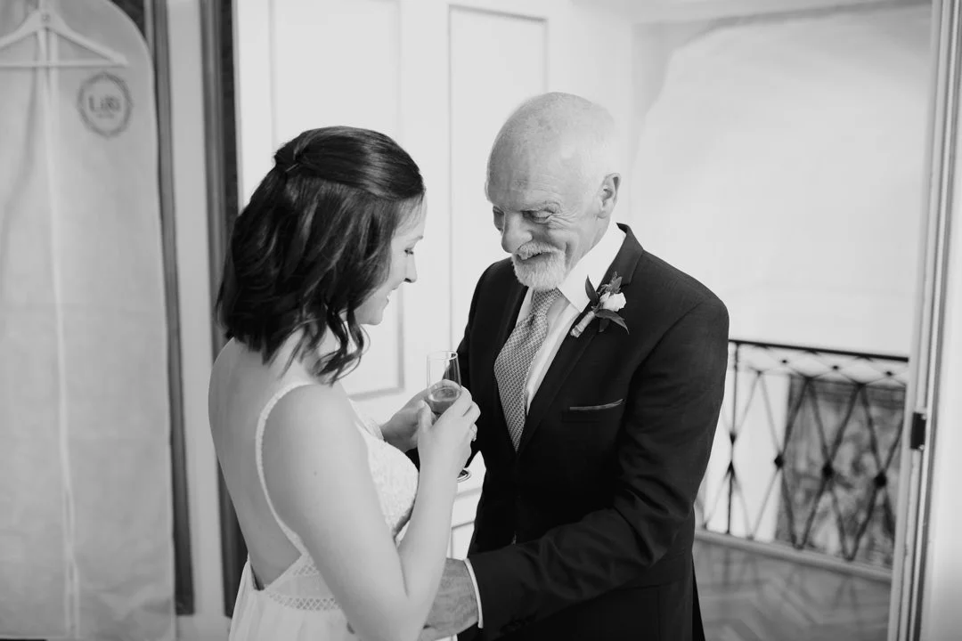 A young woman and an older man, likely at a wedding, share a special moment with the woman holding a glass and the man holding her hand.