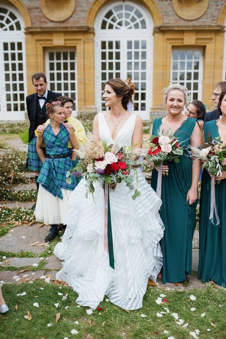 bride holding red and white flowers stood in garden, Hestercombe House Taunton