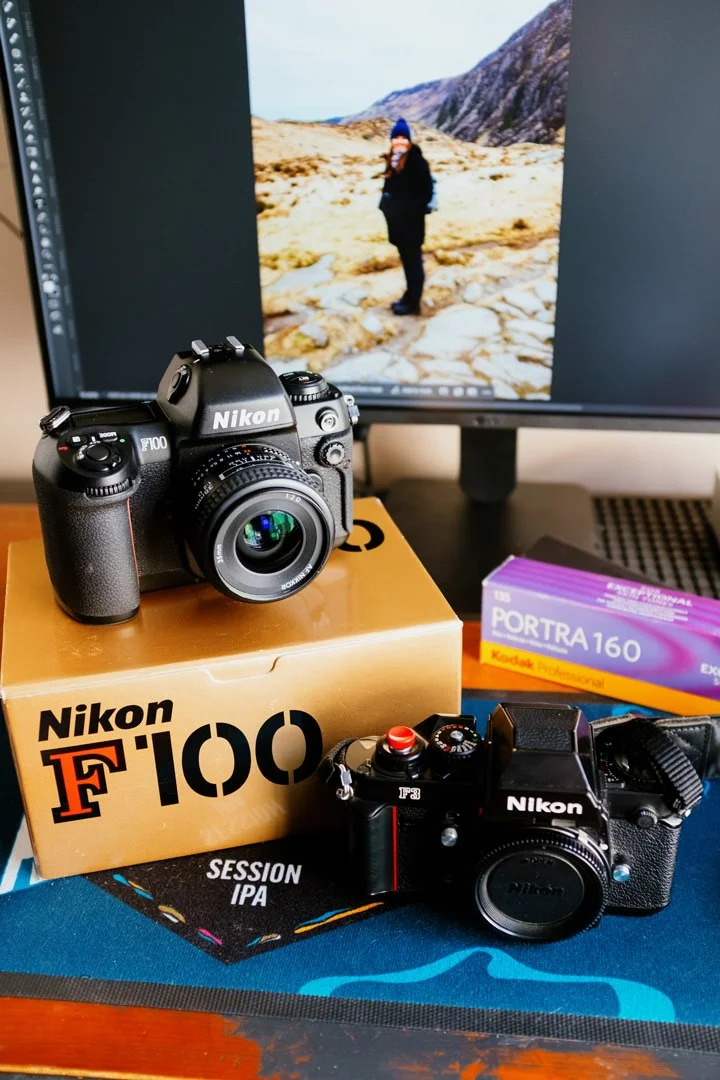 A Nikon F100 film camera, a professional Nikon F3 camera, a box of Kodak Portra 160 film, and a camera strap with