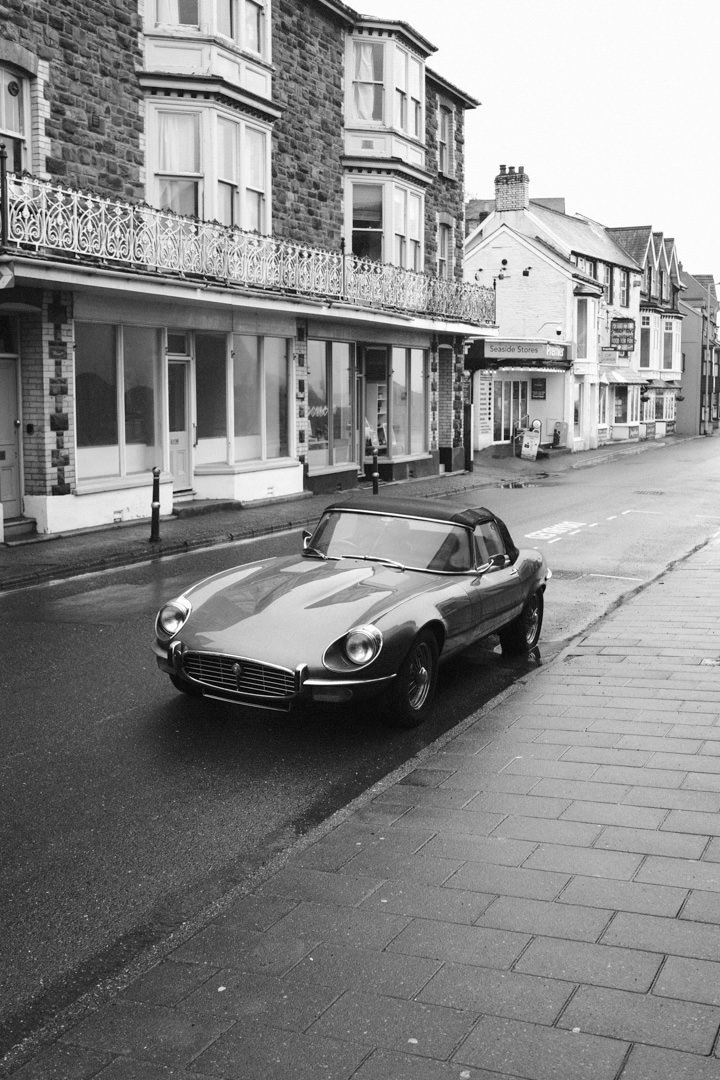 A vintage car parked on a wet street in front of historic buildings in a town or city.