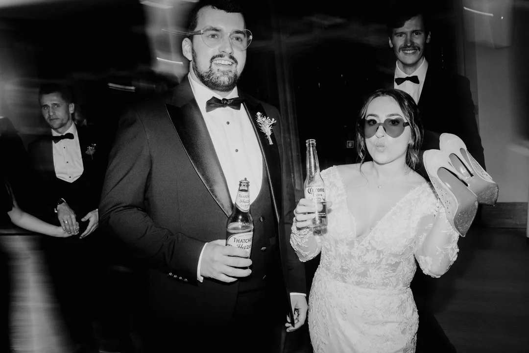bride and groom dancing holding bottles of cider waring sunglasses black and white photo