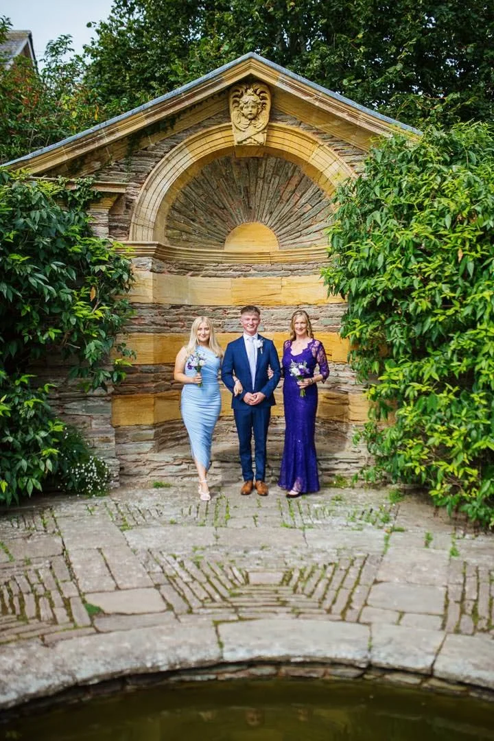 bridesmaids stood near pond in garden with flowers, Hestercombe House