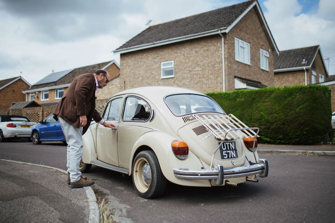 man waring a brown suit opening a door of a classic vw beetle