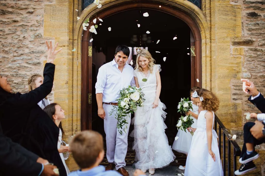 bride and groom holding large white and green flowers, they are walking towards large crowd of people