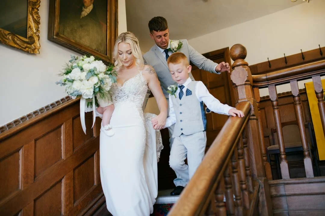 bride and groom walking down wooden stairs, they are with two children who are holding flowers