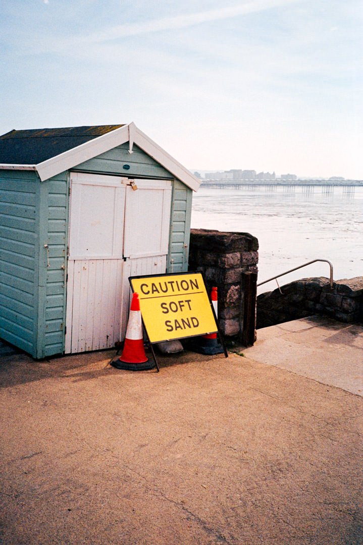 small green beach hut with traffic cone and yellow sign saying soft sand