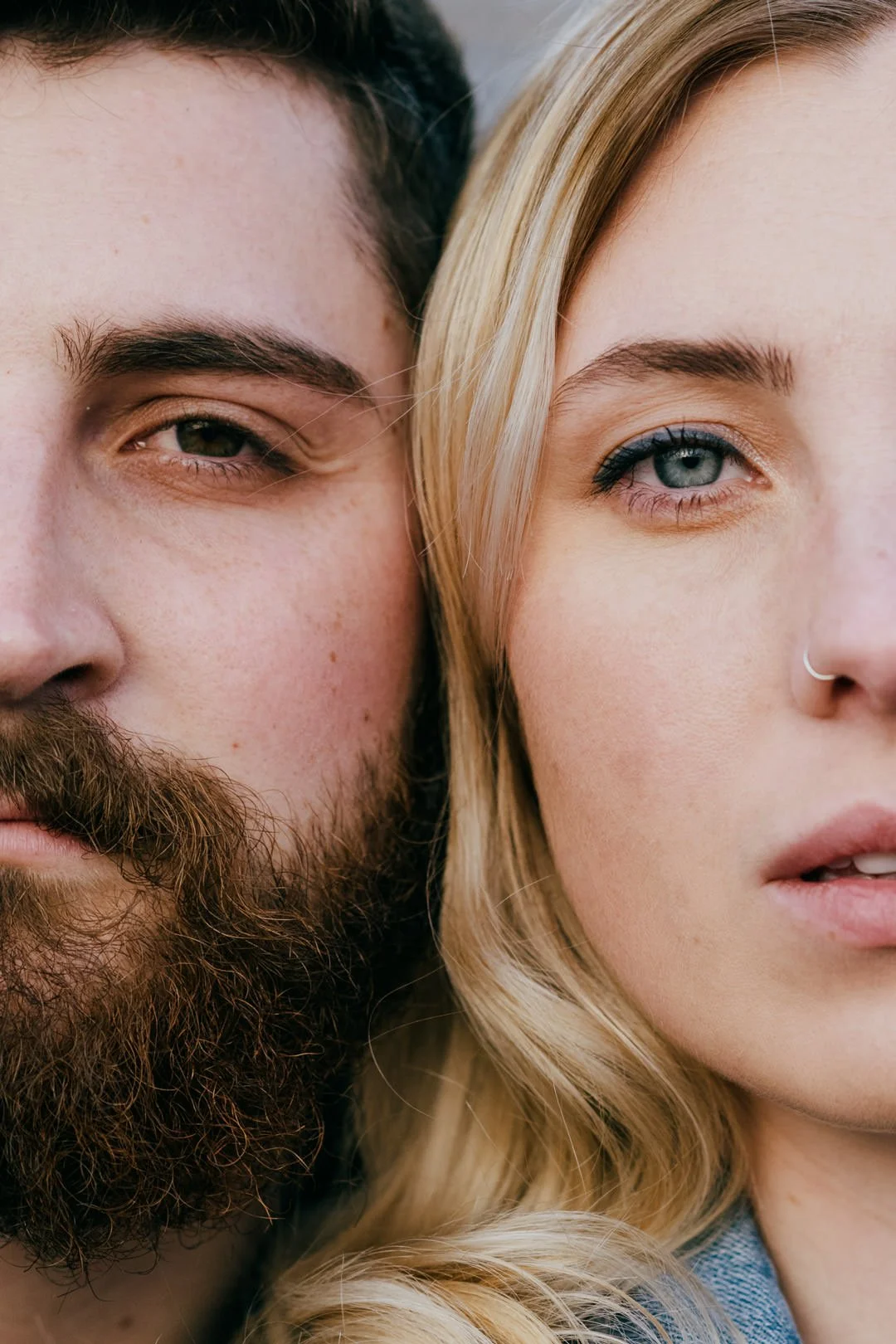 Close-up of a man and a woman with their faces nearly touching, showing only parts of their faces, including one eye each, with neutral expressions.