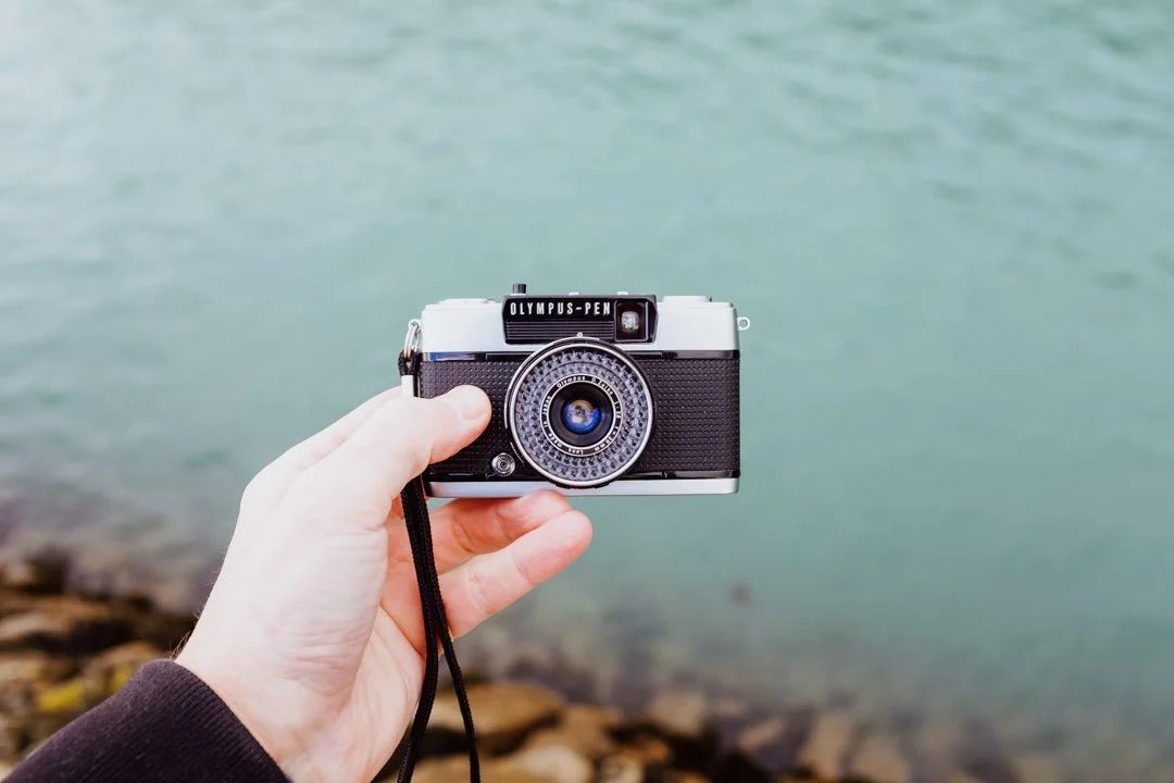 hand holding small camera above blue water, Olympus Pen ees2
