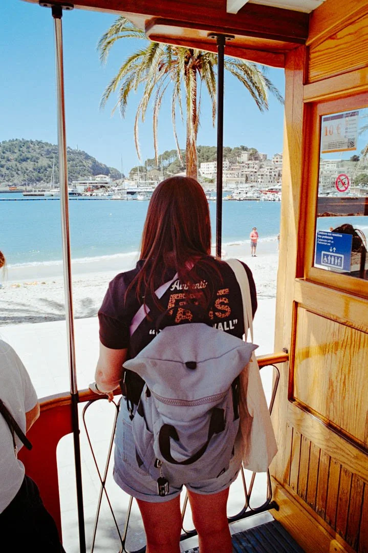 girl waring vans t shirt and purple ruck sack looking towards ocean and mountains