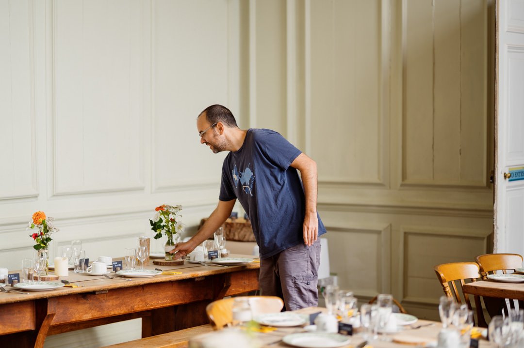 man in blue shirt filling vases on table with wedding flowers