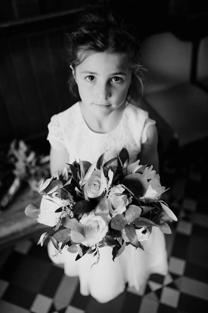 small girl in white dress holding a large bunch of wedding flowers