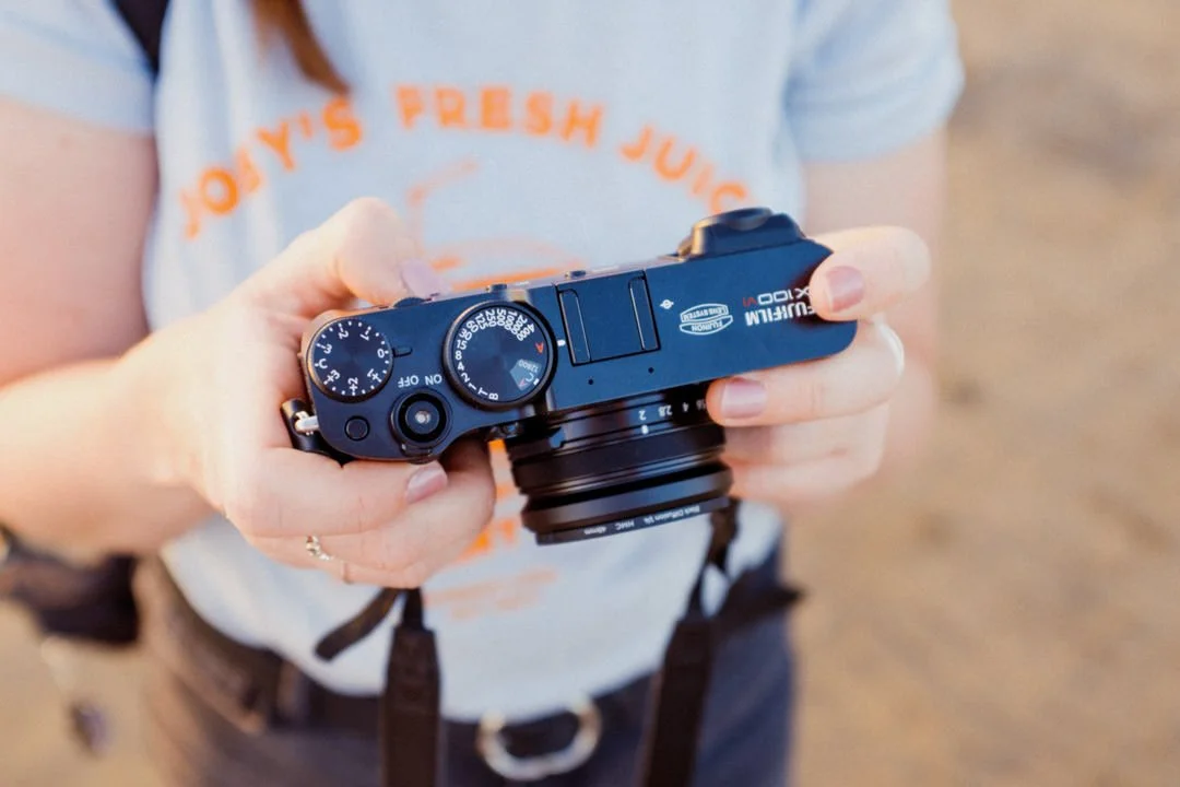 Person holding a black digital camera, with a blurred background.