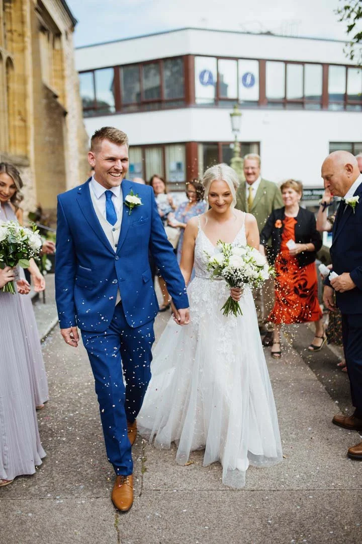 bride and groom holding hands walking through white confetti