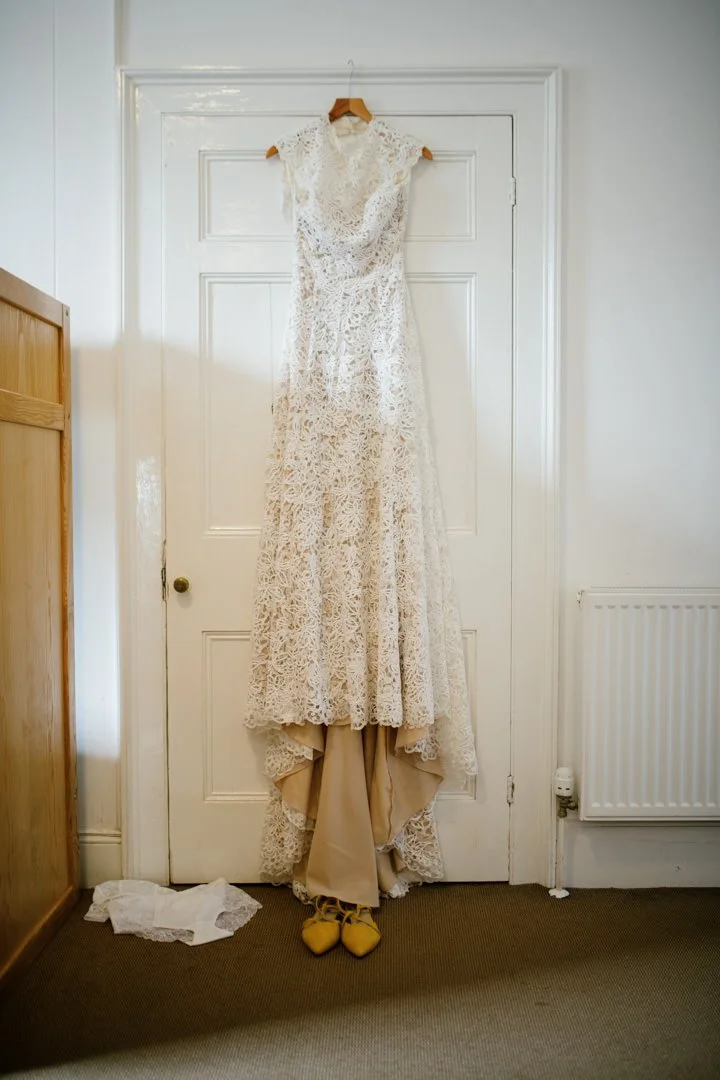 traditional wedding dress hanging from door frame with yellow shoes