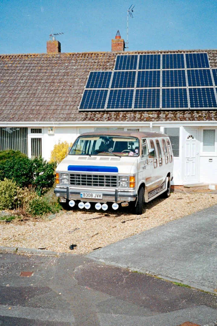 Chevrolet camper van with chrome bumper on driveway, there are solar panels on the roof of the house