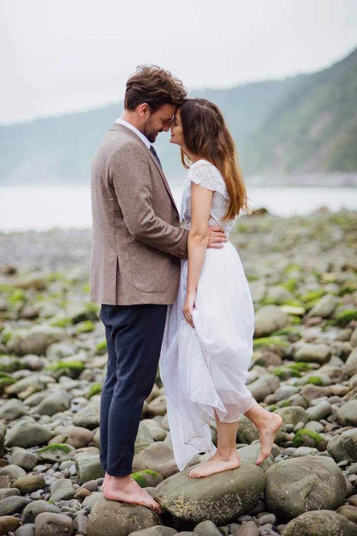 bride and groom stood on misty beach embracing and smiling