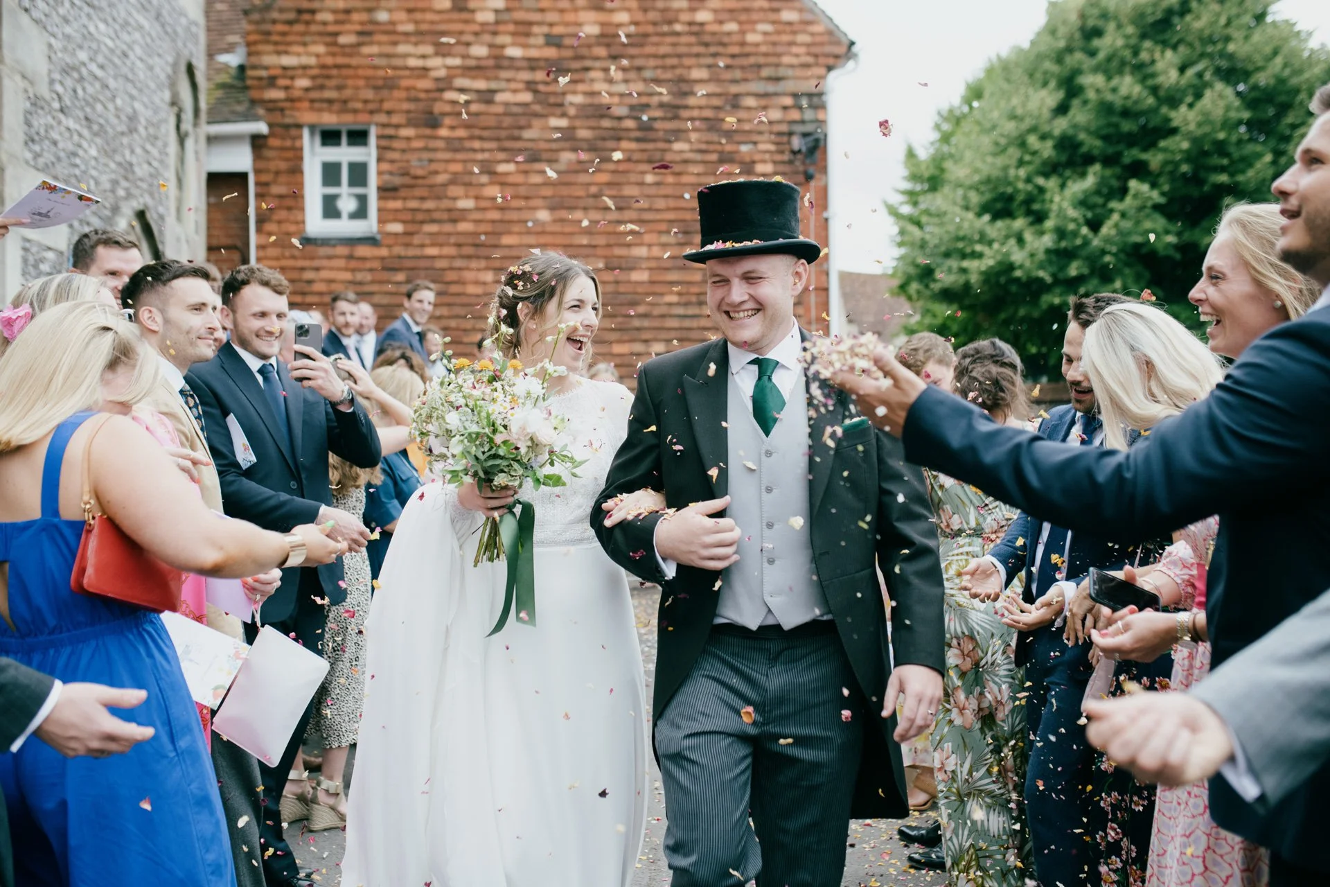 A bride and groom walking through a crowd of celebrating guests at their outdoor wedding, with confetti falling around them.