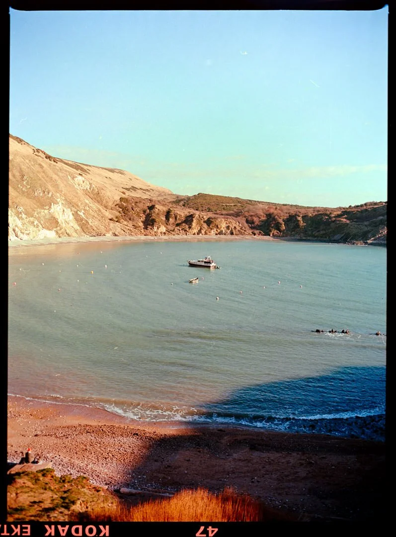 small boat on blue water with cliffs behind, lulworth cove Dorset