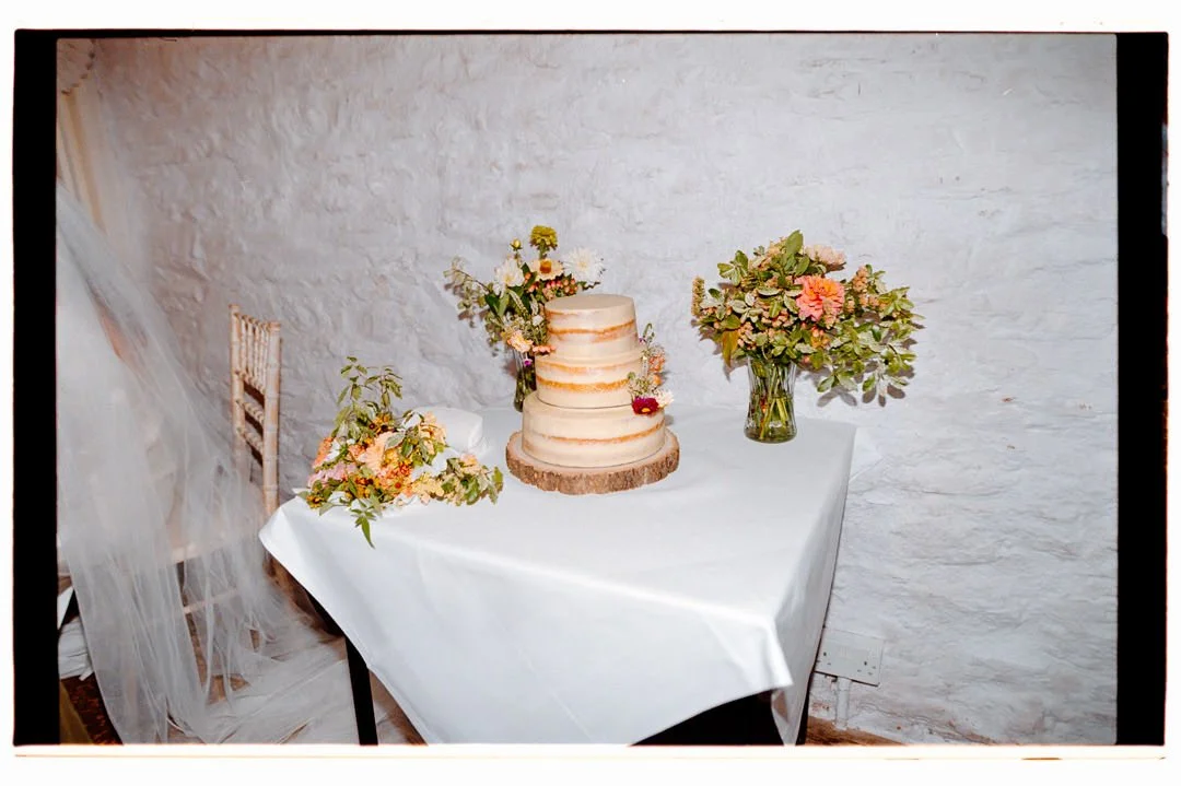 A wedding cake on a table with floral decorations and vases, set against a white textured wall.