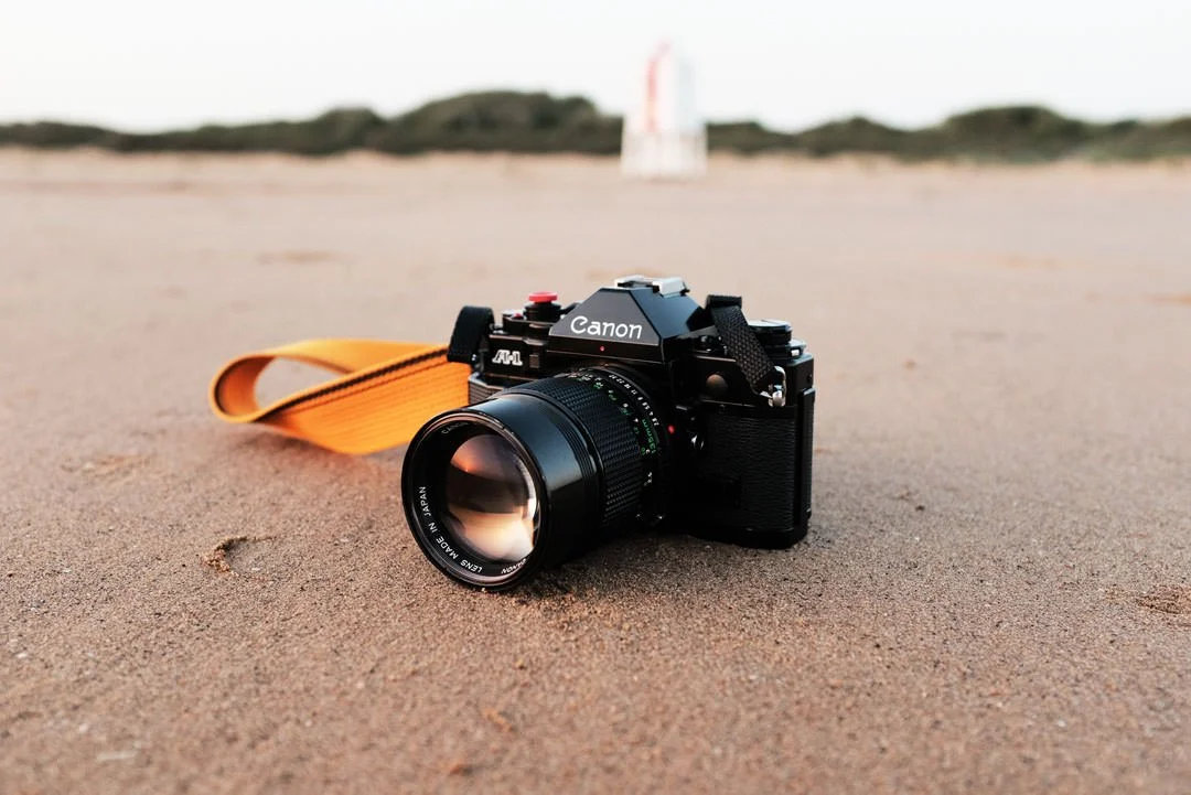 canon a1 film camera on beach with lighthouse behind during sunset, fuji x100f chrome recipe