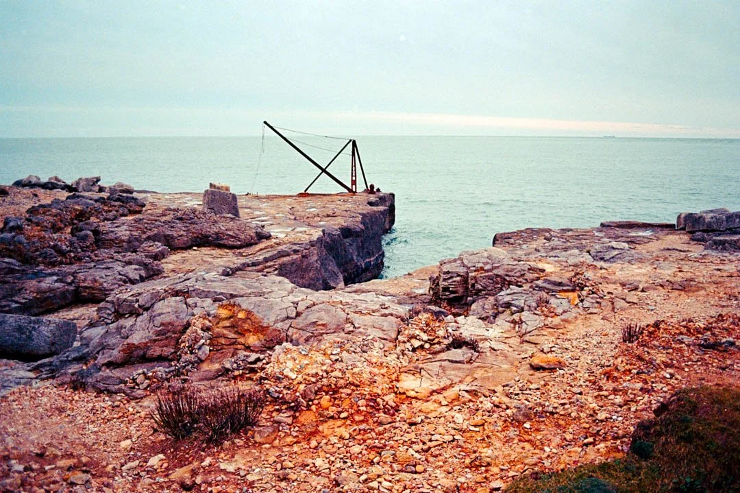 large rock formations with blue water and flowers on ground, canon a-1