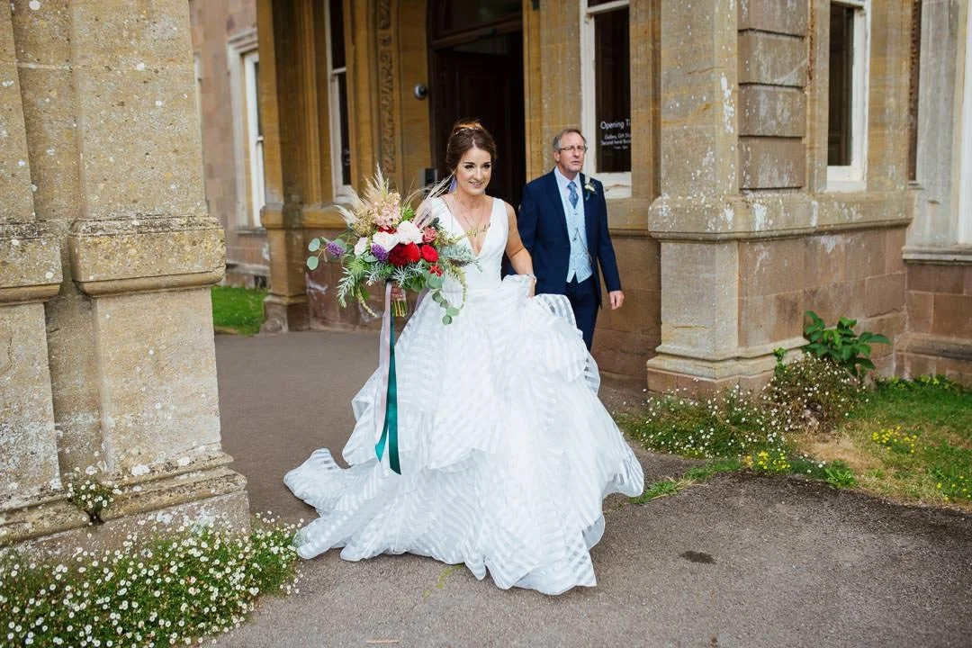 wedding bride holding white and red flowers walking with her father, hestercombe house Somerset