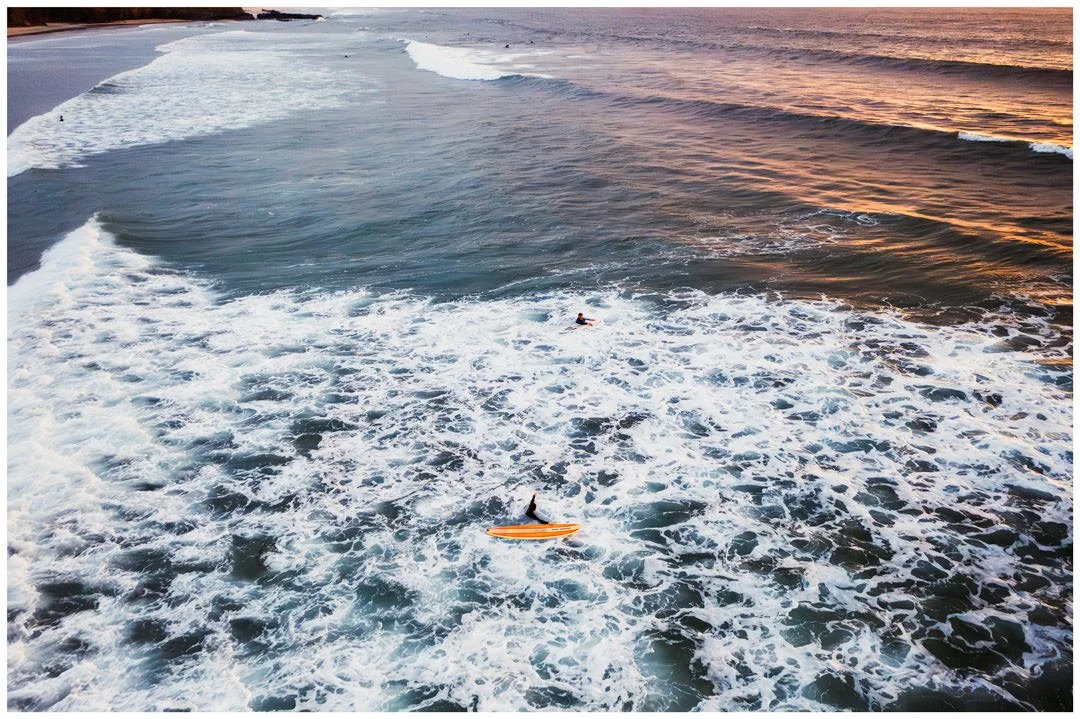 Aerial view of the ocean at sunset with surfers and surfboards in the water.