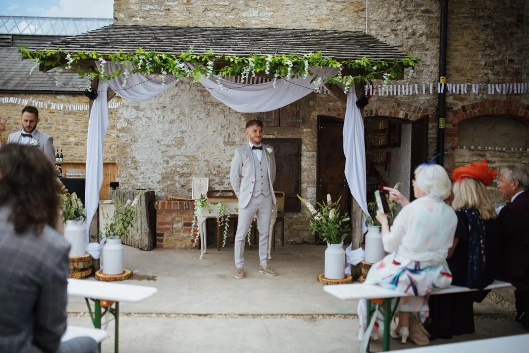 wedding groom stood under canopy. he is smiling looking towards a camera