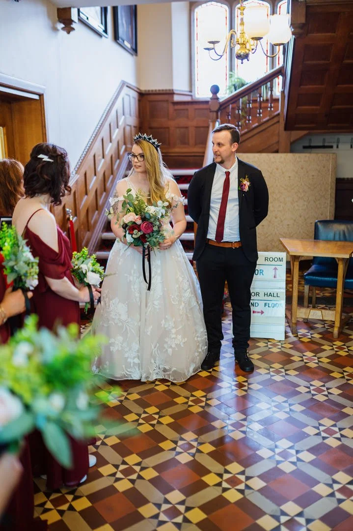 wedding bride holding red and orange flowers stood below large window