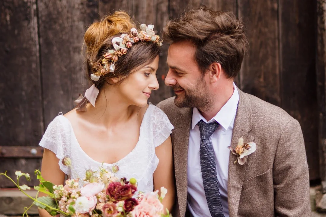 bride and groom sat on bench near barn door smiling at each other