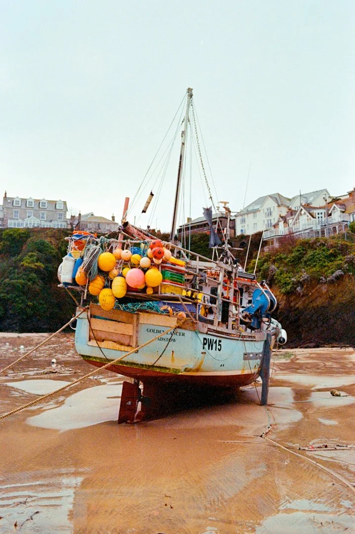 A boat resting on the sand at low tide with buildings on a hill in the background.