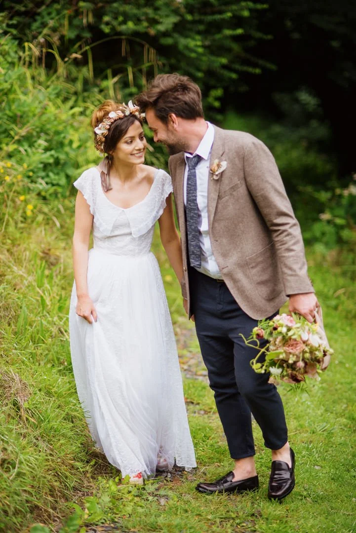 bride and groom walking near wooded area holding hands