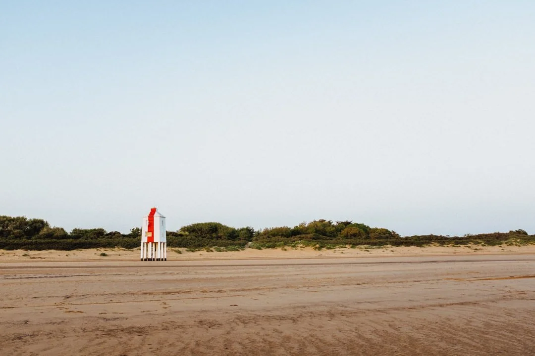 A lifeguard tower on a sandy beach with green bushes and clear sky in the background.