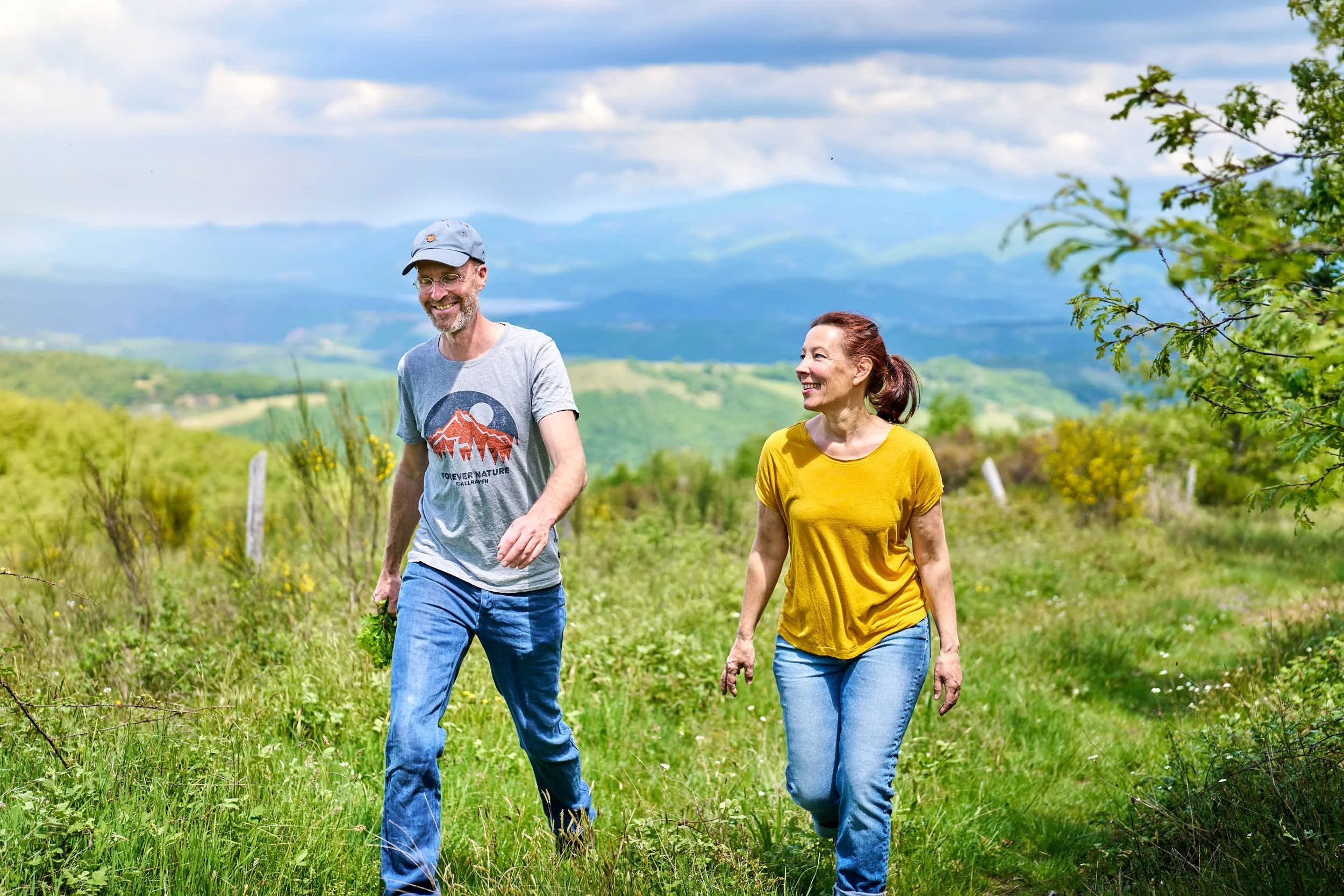 Ein Mann und eine Frau wandern in einer grünen, offenen Landschaft bei schönem Wetter.