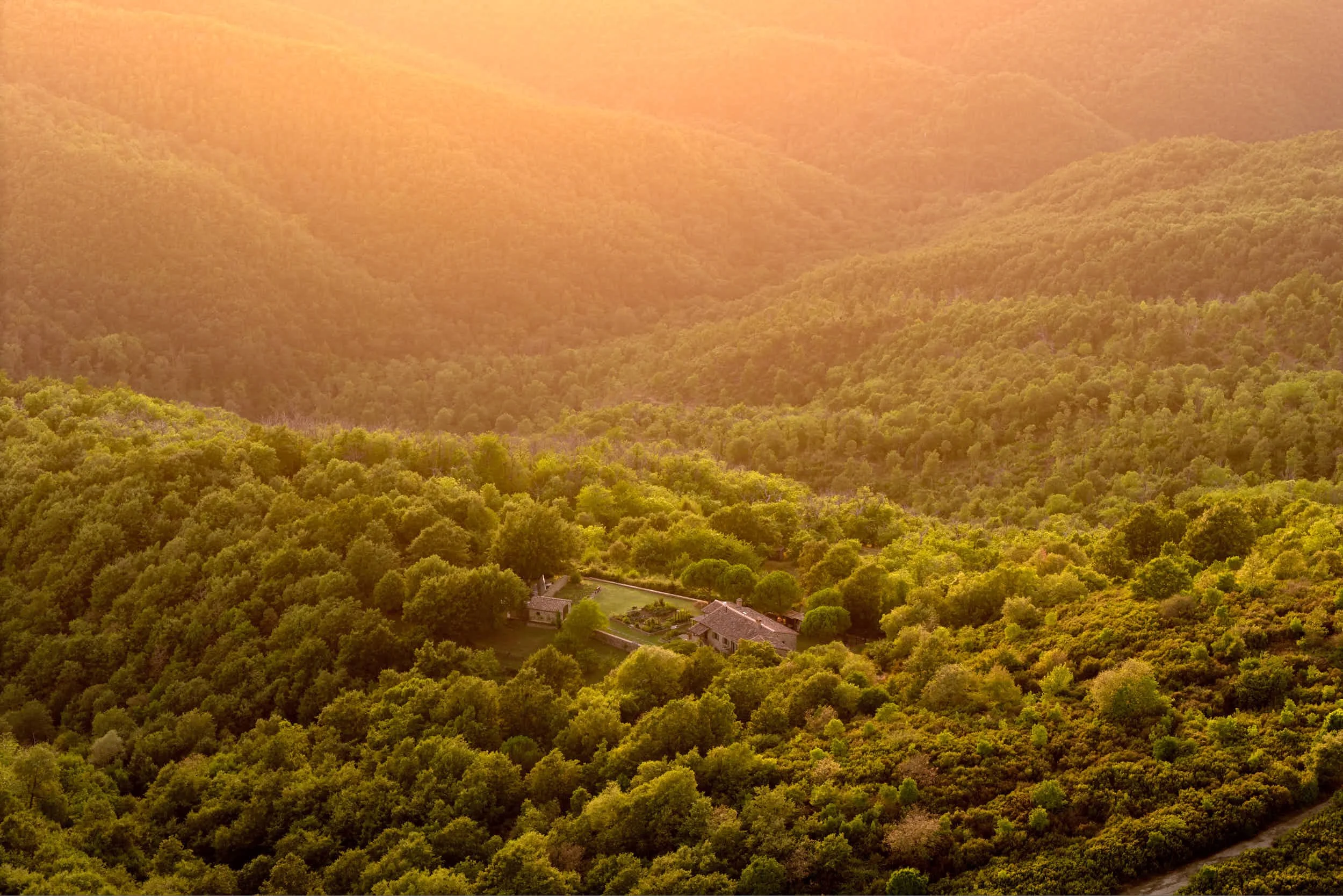 Landschaft mit grünen Hügeln, Bäumen und einem Haus bei Sonnenuntergang.