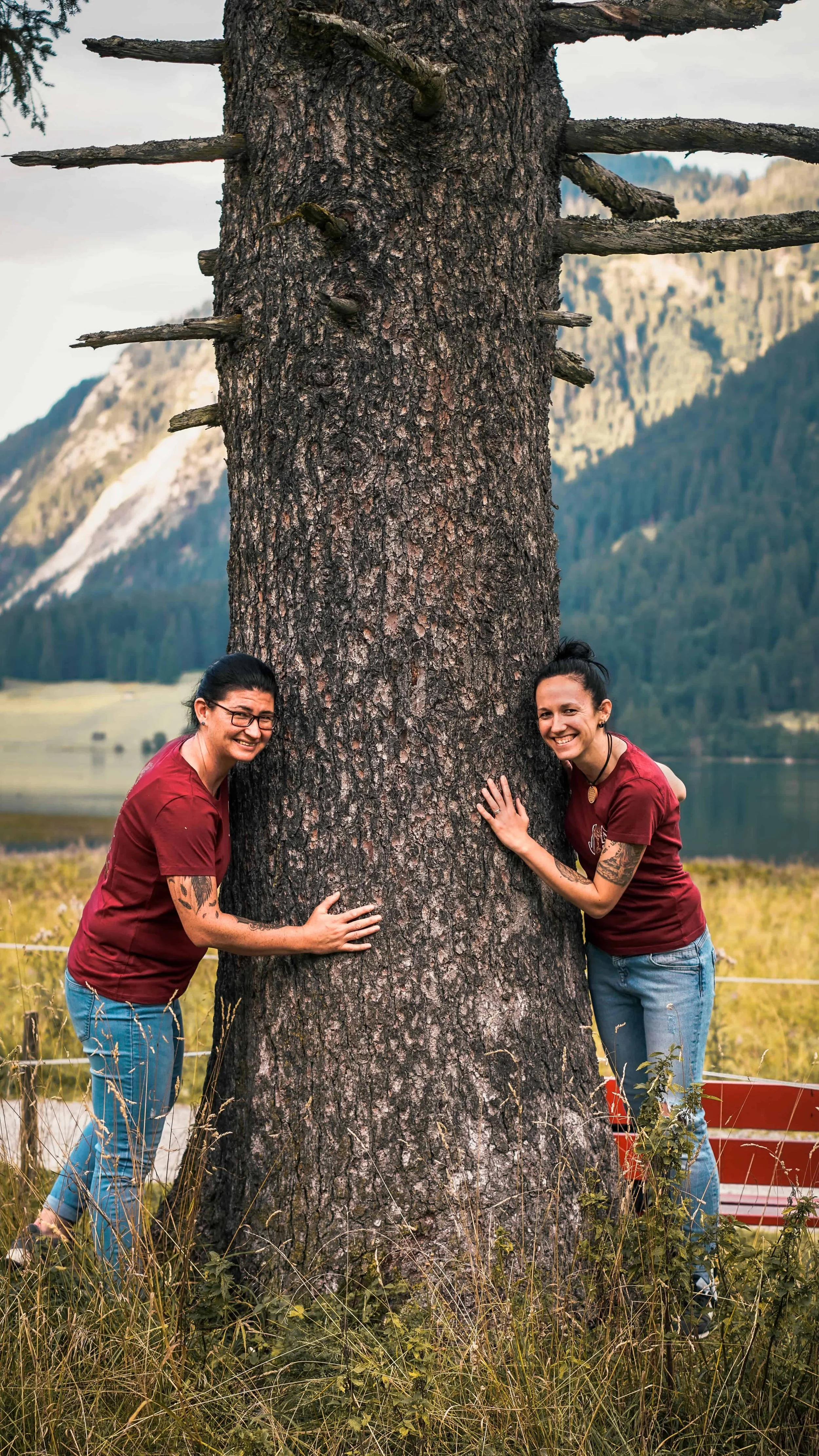Janine Ruske & Sandy Hübner vom Seelenkraft Raum Nesselwang umarmen einen Baum in der Natur des Allgäus. Das Bild steht für Erdung, Verbindung und Heilung – den Weg aus Burnout, Stress und innerer Leere hin zu Lebenskraft, Leichtigkeit &  Entspannung