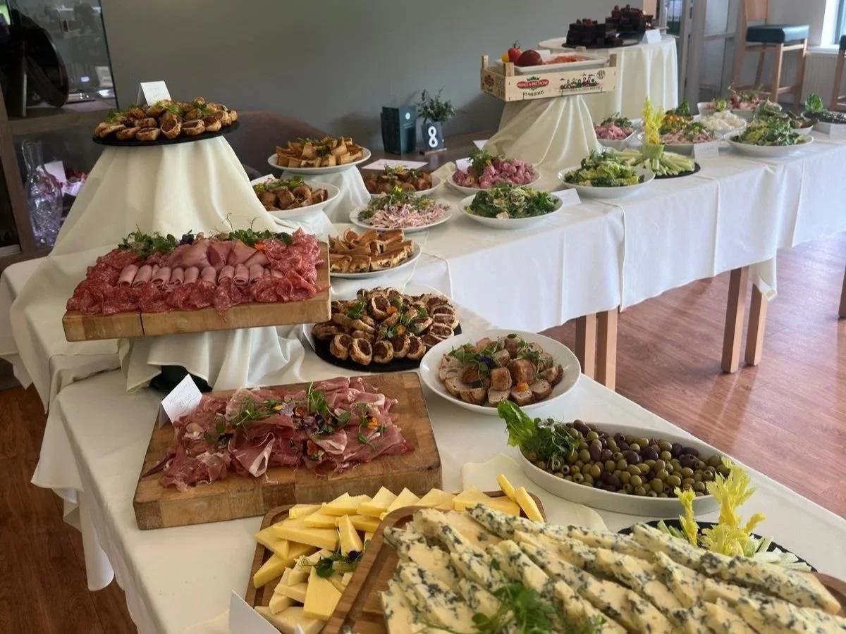 Buffet table with assorted meats, cheeses, salads, and olives at a catered event.